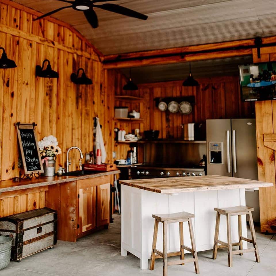 summer kitchen area with wood walls, bar with two stools, refrigerator, stove, and rustic decor